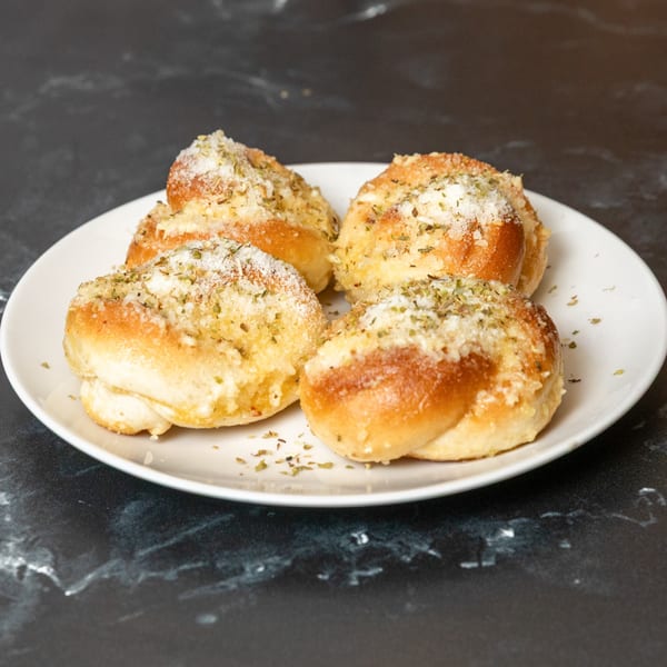 Four golden-brown garlic knots, sprinkled with herbs and parmesan cheese, on a white plate.