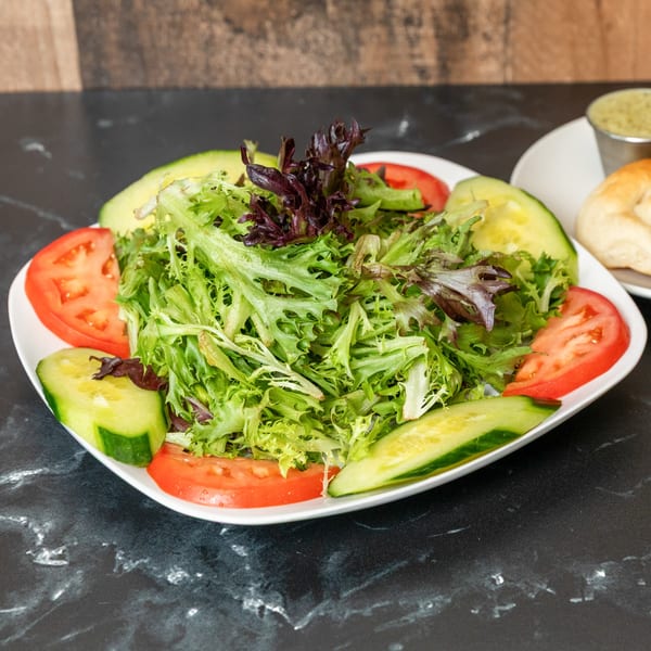 Fresh garden salad with mixed greens, sliced tomatoes, and cucumbers on a white plate.