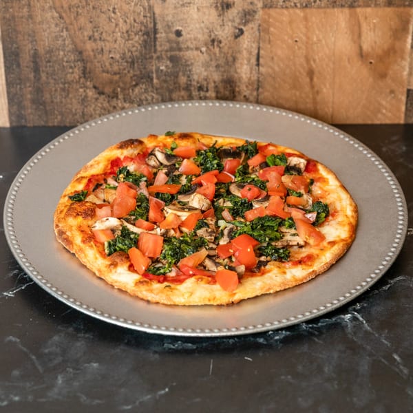 A Piccolo Pizza & More pizza with tomatoes, mushrooms, and spinach on a gray plate.
