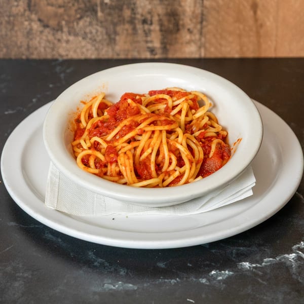 A white bowl of spaghetti with red tomato sauce, served on a white plate with a napkin.